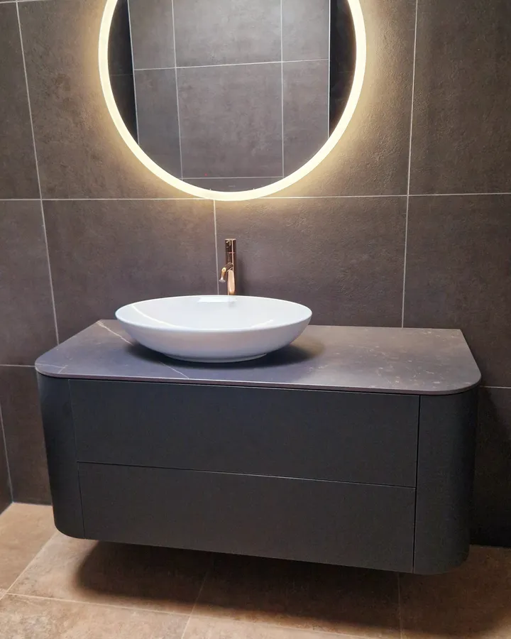 Salle de bains avec meuble vasque, miroir rond lumineux et carrelage minéral