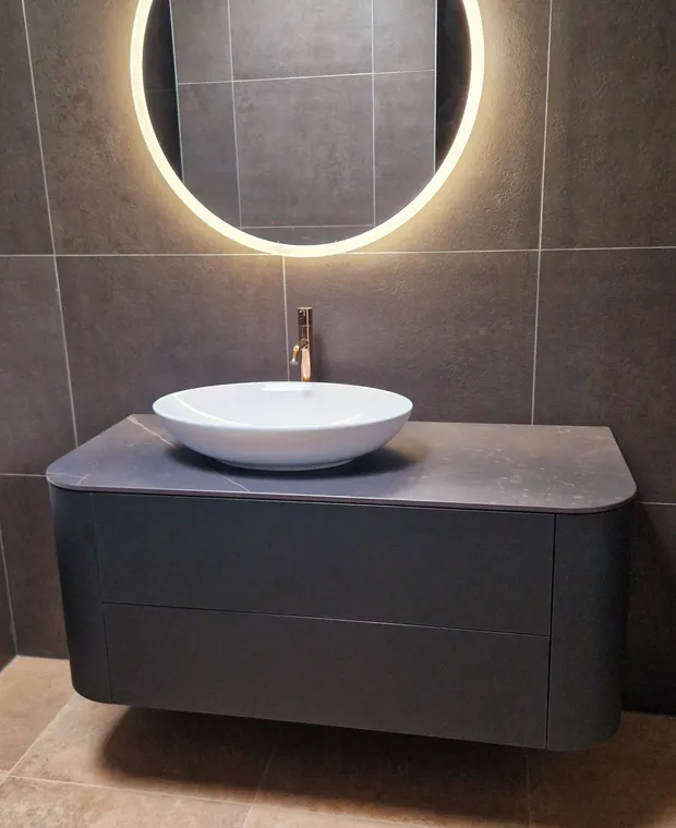 Salle de bains avec meuble vasque, miroir rond lumineux et carrelage minéral