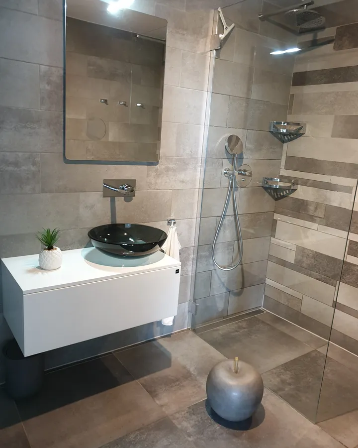 Espace douche avec paroi vitrée, vasque noire et carrelage minéral